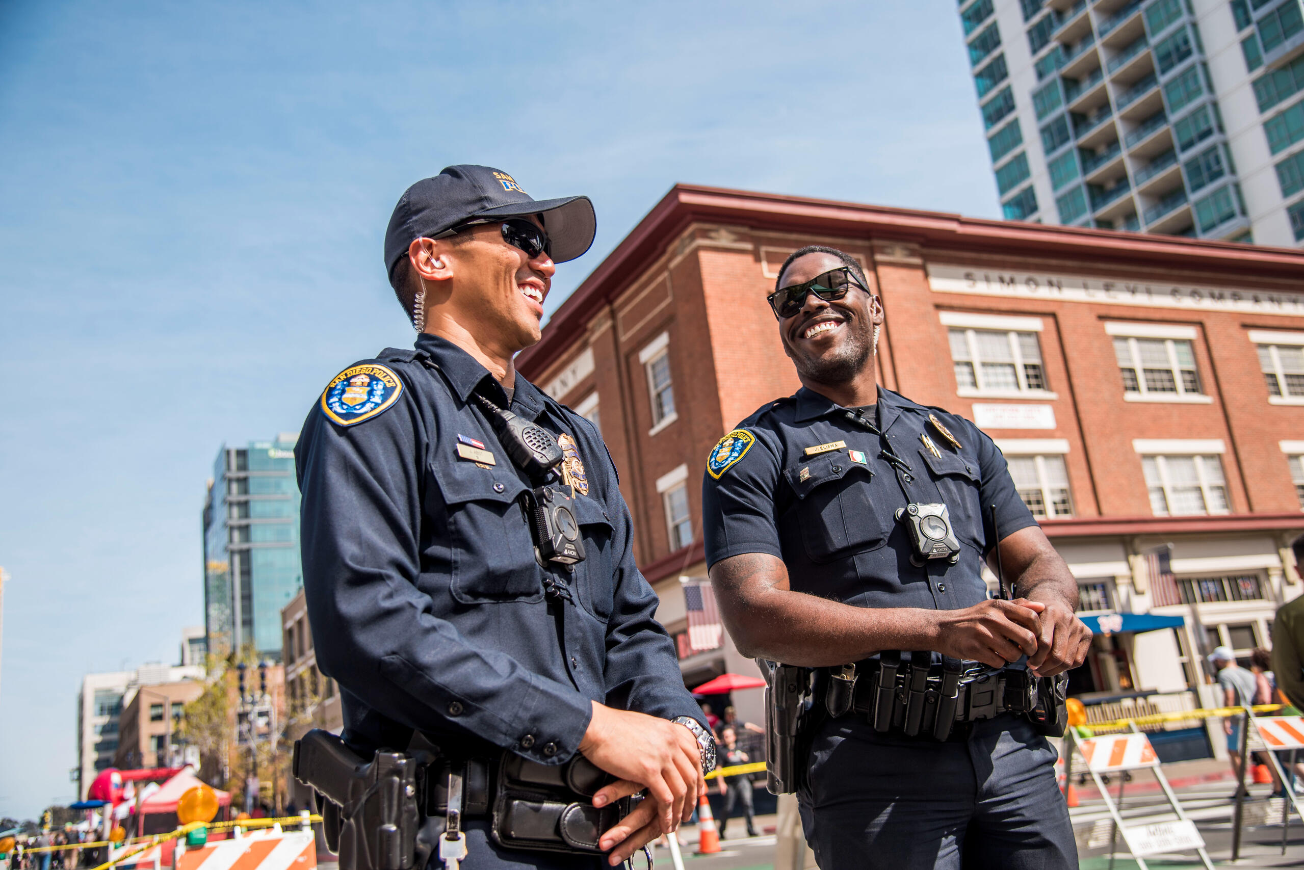Two police officers laughing during a community event in downtown San Diego, captured in a candid moment of connection and ease.