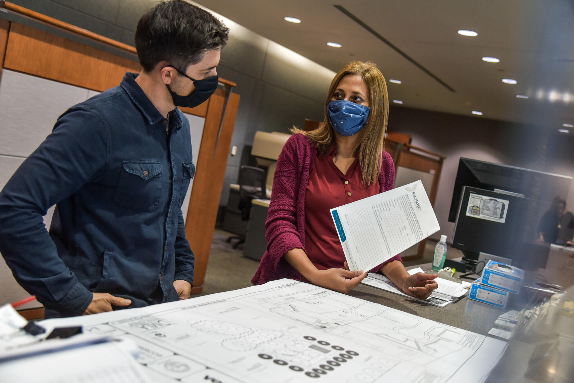City employees collaborating over architectural plans inside a municipal office—documentary-style capture of public sector coordination during COVID protocols.