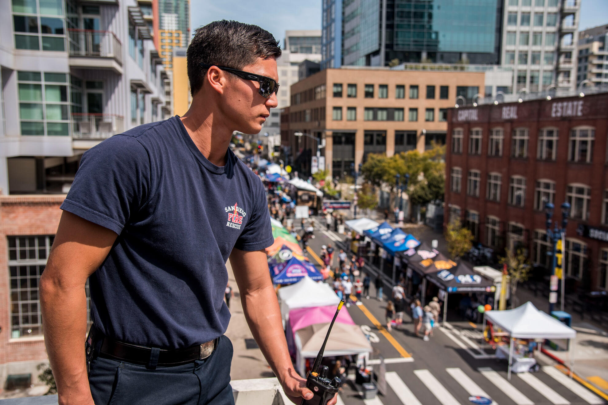 Firefighter overseeing street event from above during downtown San Diego safety activation—shot highlights civic presence, crowd energy, and clean urban lines.